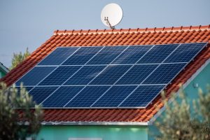 Close-up of solar panels installed on houses red tiled roof with satellite dish, natural landscape. Represents clean energy, rural technology integration. Photovoltaic system on roof.